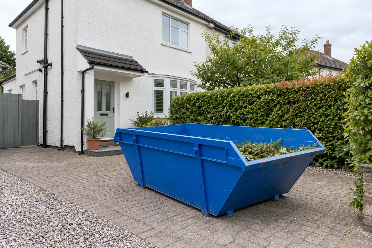 Blue skip with a low load of garden cuttings beside a house