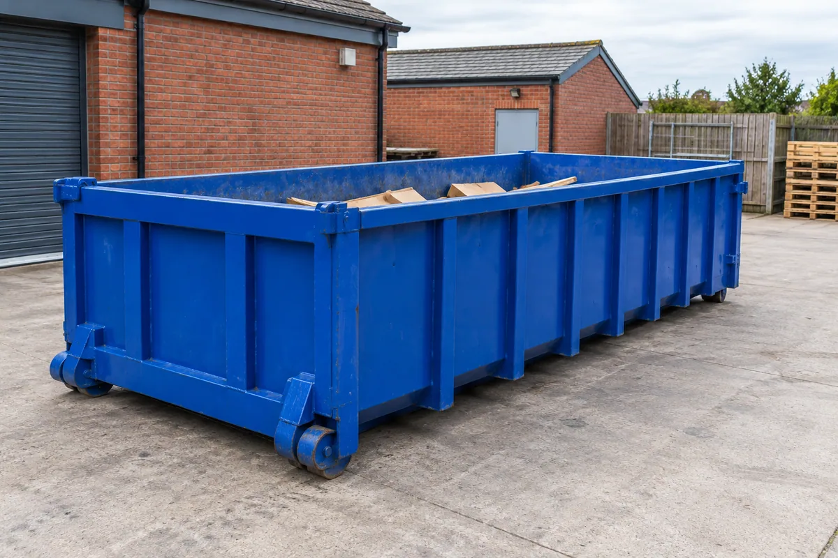 Blue roll-on/off container beside a brick workshop